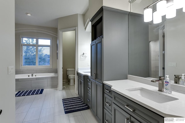 bathroom with a relaxing tiled tub, tile patterned floors, vanity, and toilet