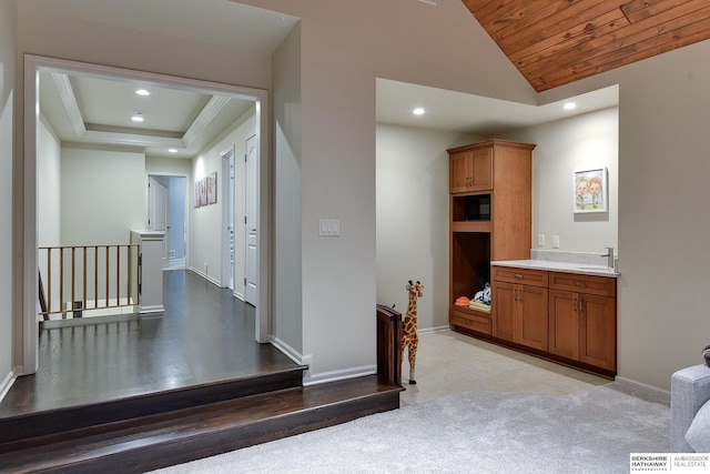 hallway featuring sink, wood ceiling, vaulted ceiling, a raised ceiling, and light colored carpet