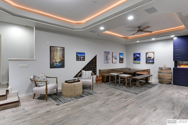 recreation room with ceiling fan, a tray ceiling, and light wood-type flooring