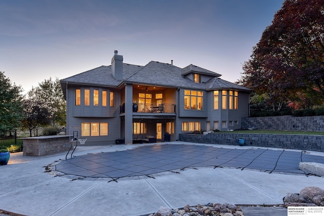 back house at dusk featuring a covered pool, a patio area, and a balcony