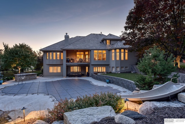 back house at dusk featuring a patio and a balcony