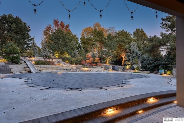 pool at dusk featuring a patio and a water slide