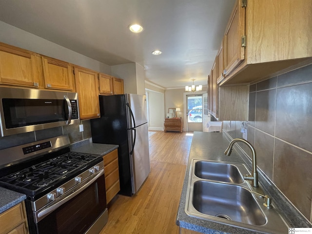 kitchen featuring sink, appliances with stainless steel finishes, an inviting chandelier, backsplash, and light wood-type flooring
