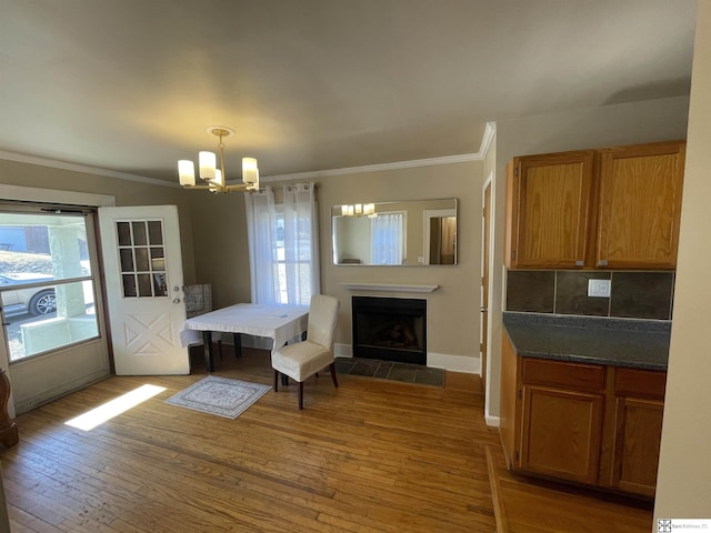 dining area featuring an inviting chandelier, ornamental molding, wood-type flooring, and a tiled fireplace