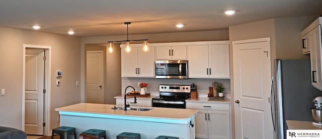 kitchen with sink, a kitchen island with sink, hanging light fixtures, stainless steel appliances, and white cabinets