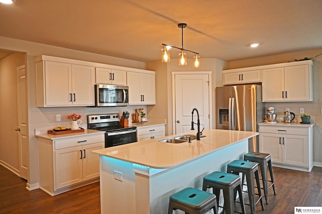 kitchen with sink, white cabinets, hanging light fixtures, a kitchen island with sink, and stainless steel appliances