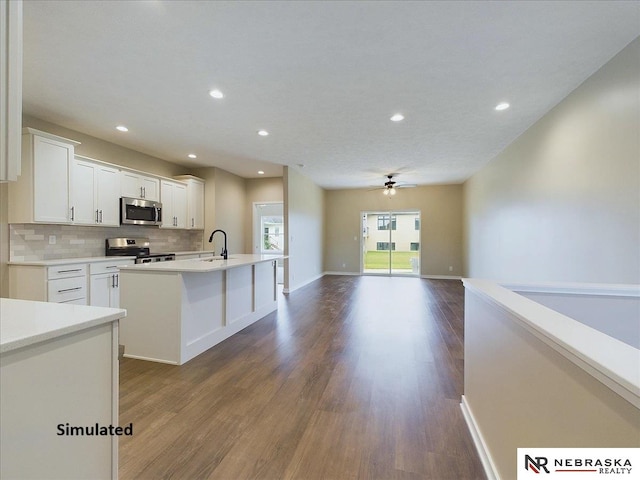 kitchen with backsplash, stainless steel appliances, a center island with sink, and white cabinets