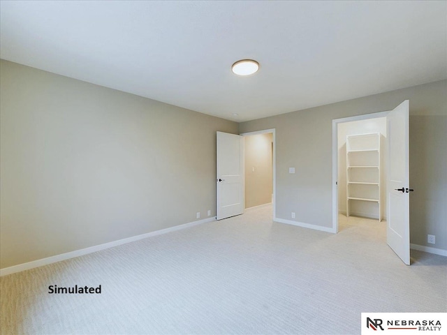 unfurnished bedroom featuring a walk in closet, light carpet, and baseboards