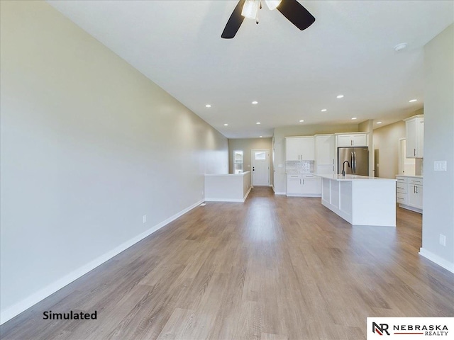 unfurnished living room featuring light wood finished floors, recessed lighting, a sink, and baseboards