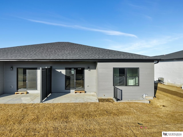 rear view of property with a patio area, a shingled roof, central AC unit, and a yard