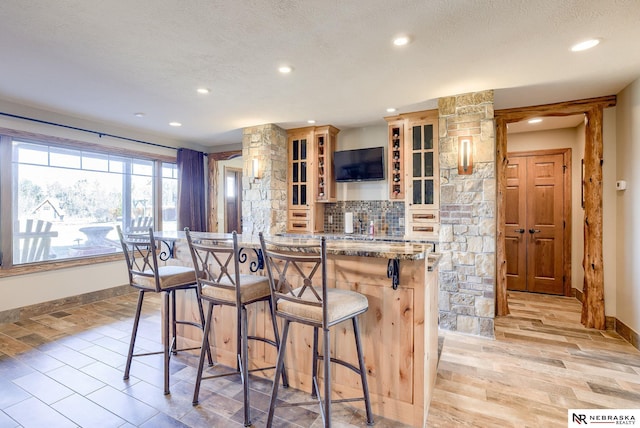 kitchen with backsplash, a kitchen breakfast bar, light stone counters, a textured ceiling, and light wood-type flooring