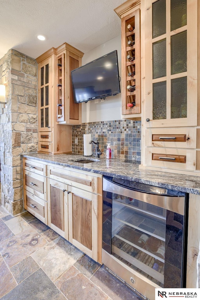 kitchen featuring stone counters, sink, beverage cooler, decorative backsplash, and a textured ceiling