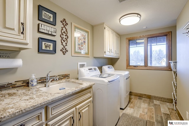 clothes washing area with cabinets, washing machine and dryer, sink, and light hardwood / wood-style flooring