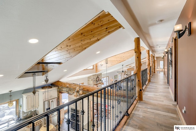 hall with lofted ceiling, a wealth of natural light, wood walls, and light wood-type flooring