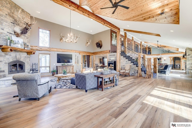 living room featuring a fireplace, ceiling fan with notable chandelier, beam ceiling, and light hardwood / wood-style flooring