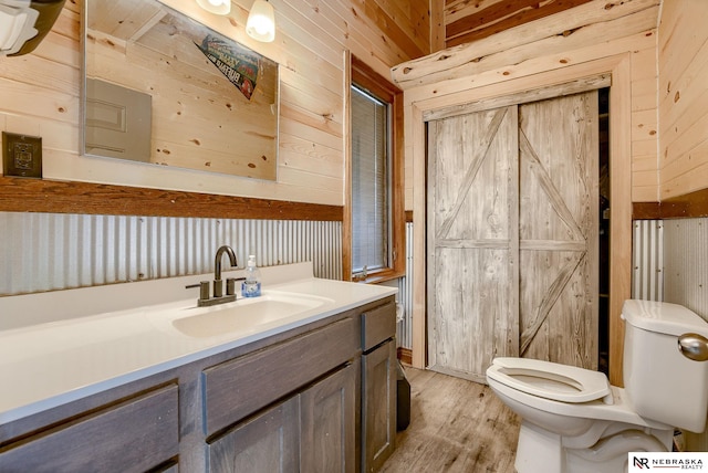 bathroom featuring hardwood / wood-style flooring, toilet, vanity, and wood walls