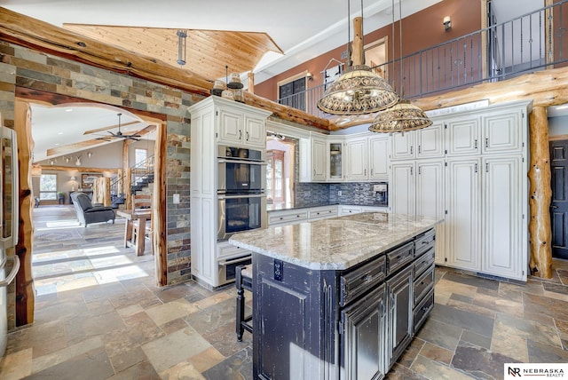 kitchen with a kitchen island, stainless steel double oven, white cabinets, and decorative light fixtures