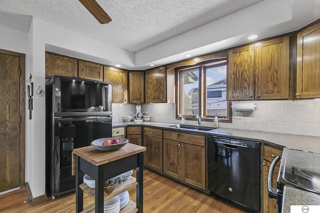 kitchen featuring sink, backsplash, black appliances, a textured ceiling, and light wood-type flooring