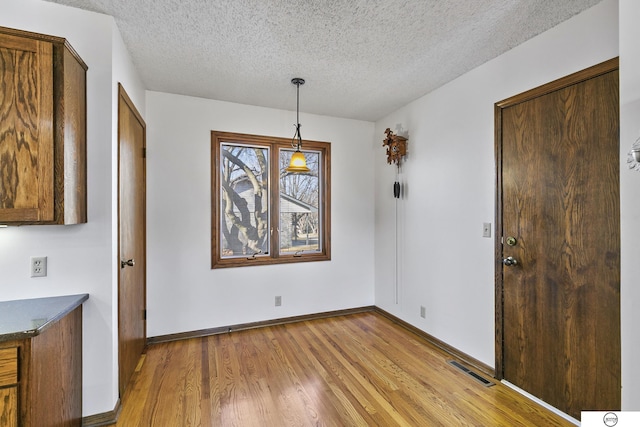 unfurnished dining area featuring light hardwood / wood-style flooring and a textured ceiling