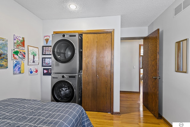 bedroom with stacked washer / drying machine, light hardwood / wood-style flooring, a closet, and a textured ceiling