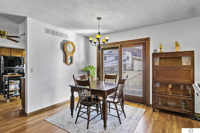 dining room featuring ceiling fan with notable chandelier, a textured ceiling, and light wood-type flooring