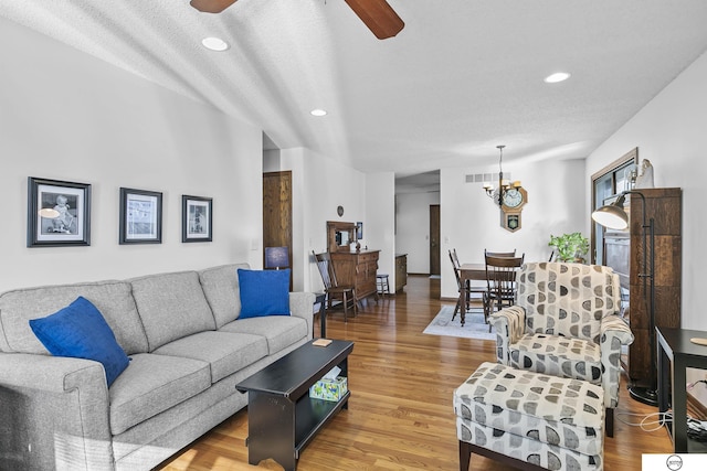 living room featuring wood-type flooring, ceiling fan with notable chandelier, and a textured ceiling