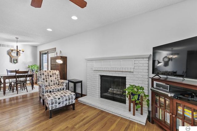 living room with a fireplace, ceiling fan with notable chandelier, and wood-type flooring