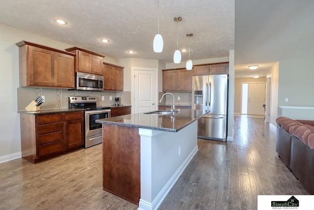 kitchen featuring appliances with stainless steel finishes, pendant lighting, an island with sink, sink, and light hardwood / wood-style flooring