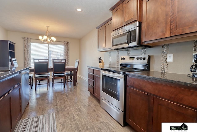 kitchen featuring an inviting chandelier, hanging light fixtures, light hardwood / wood-style flooring, appliances with stainless steel finishes, and dark stone counters