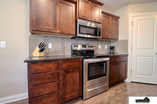 kitchen with stainless steel appliances, light hardwood / wood-style floors, decorative backsplash, and dark stone counters