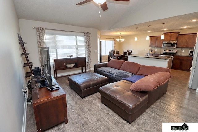 living room with light hardwood / wood-style flooring, ceiling fan with notable chandelier, and vaulted ceiling