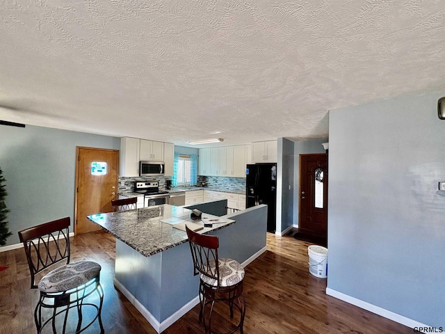 kitchen featuring dark wood-type flooring, appliances with stainless steel finishes, white cabinetry, tasteful backsplash, and a kitchen island