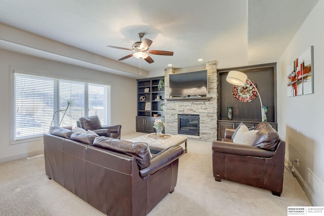 living area with a stone fireplace, built in shelves, a ceiling fan, and baseboards