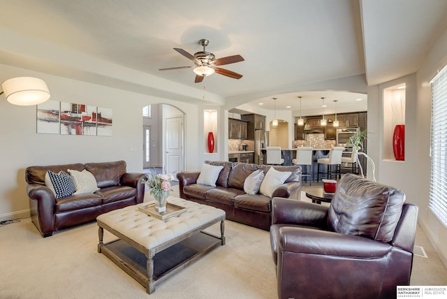 living room with arched walkways, baseboards, light carpet, and a ceiling fan