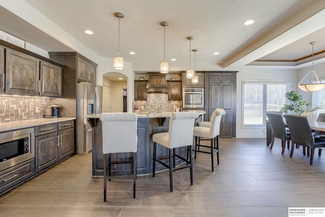 kitchen featuring premium range hood, a kitchen bar, decorative light fixtures, stainless steel appliances, and arched walkways