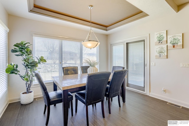 dining space featuring visible vents, a raised ceiling, baseboards, and wood finished floors