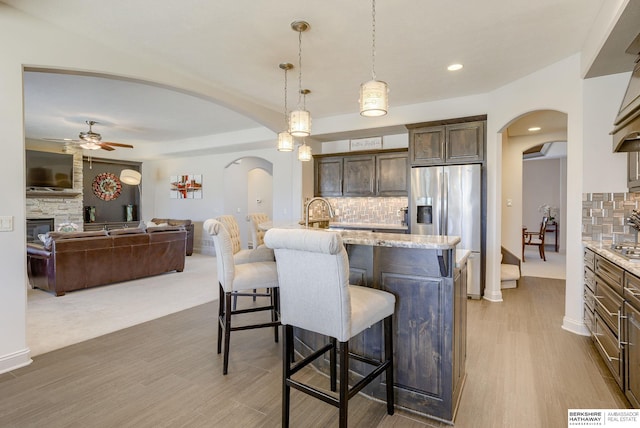 kitchen featuring dark brown cabinets, a breakfast bar, a fireplace, arched walkways, and stainless steel fridge