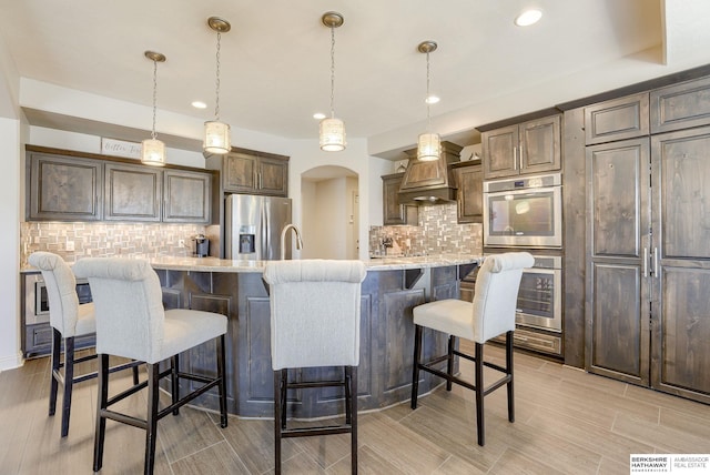 kitchen featuring a kitchen bar, decorative backsplash, arched walkways, custom exhaust hood, and stainless steel appliances