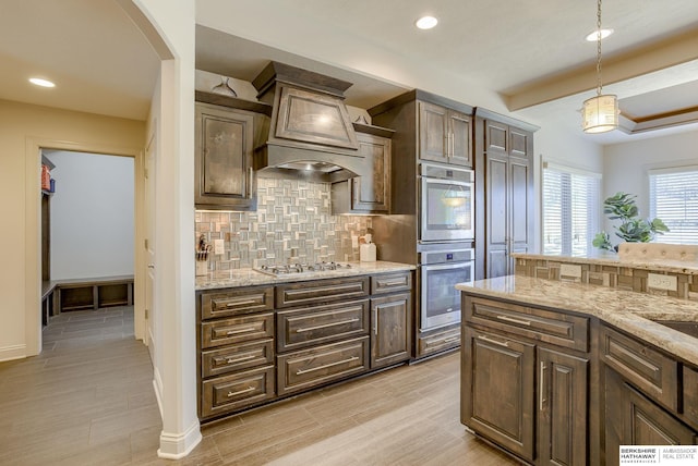 kitchen featuring pendant lighting, tasteful backsplash, stainless steel appliances, dark brown cabinetry, and light stone countertops