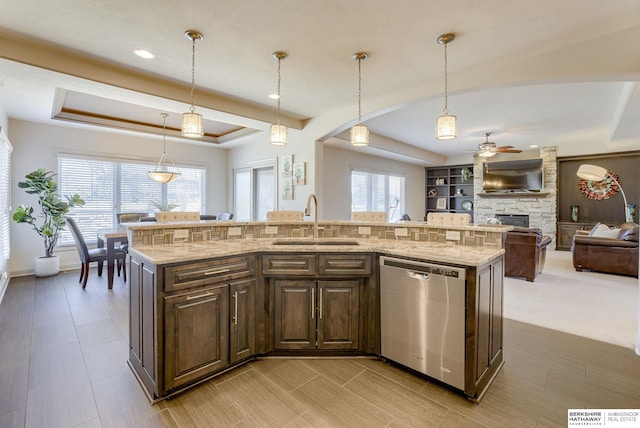 kitchen with light stone countertops, a stone fireplace, stainless steel dishwasher, a raised ceiling, and a sink