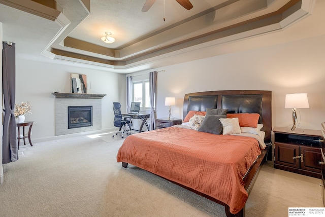 bedroom featuring a raised ceiling, light carpet, a glass covered fireplace, and a ceiling fan