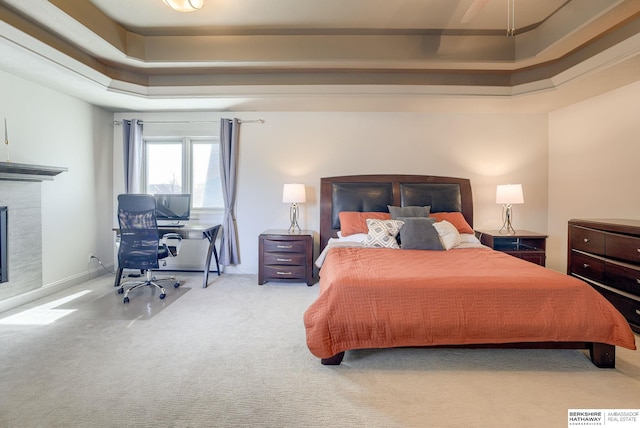 carpeted bedroom with a glass covered fireplace, baseboards, and a tray ceiling