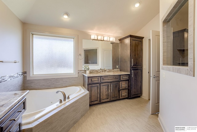 bathroom with a jetted tub, vanity, and vaulted ceiling