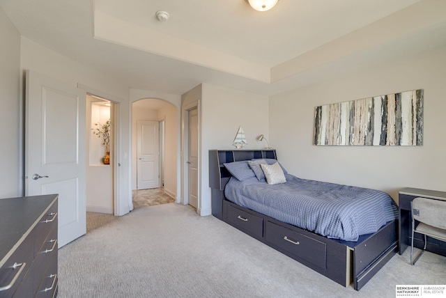 bedroom with light colored carpet, a raised ceiling, arched walkways, and baseboards