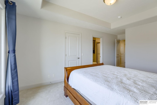 bedroom with light colored carpet, baseboards, and a tray ceiling