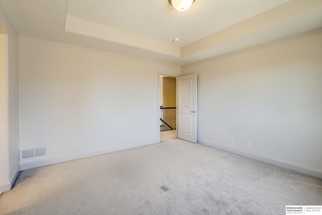 spare room featuring baseboards, a raised ceiling, light carpet, and visible vents