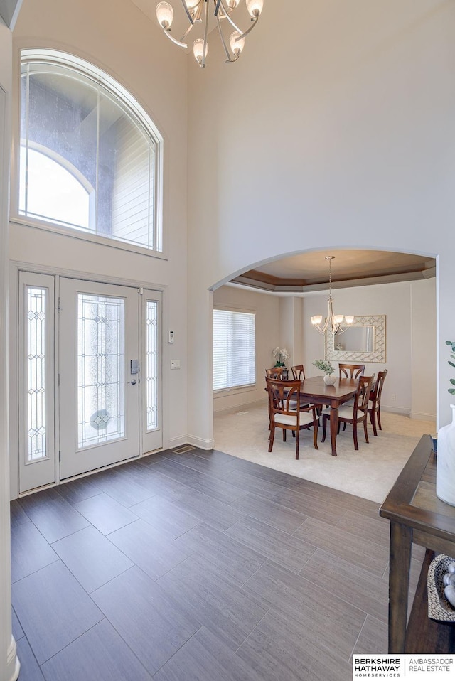 foyer featuring arched walkways, a notable chandelier, plenty of natural light, and a towering ceiling