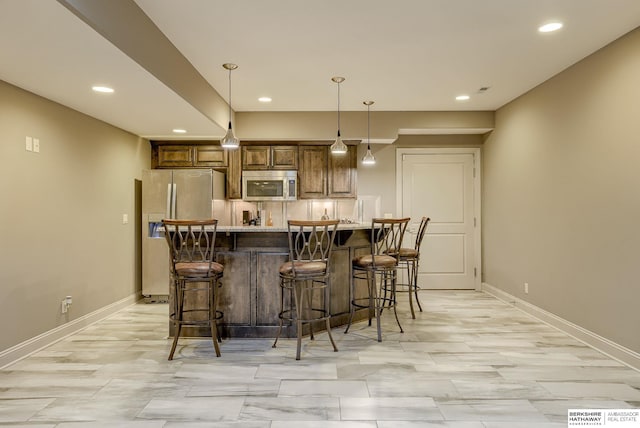 interior space featuring baseboards, pendant lighting, a kitchen bar, light countertops, and appliances with stainless steel finishes