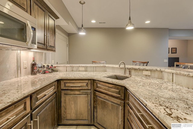 kitchen featuring stainless steel microwave, decorative light fixtures, light stone counters, recessed lighting, and a sink