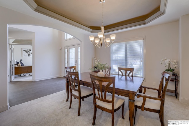 dining space featuring baseboards, a chandelier, carpet floors, arched walkways, and a raised ceiling